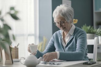 Happy elderly woman solving a puzzle and drinking tea