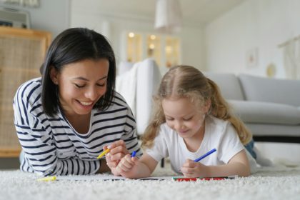 Happy mom, adopted daughter drawing together, lying on floor. Adoption, children's creative leisure